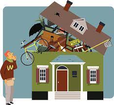 A man standing next to a house full of crap representing that he is the root cause of this bad house.
