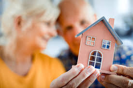 Image of an older couple holding a small house in their hands signifying they are downsizing.