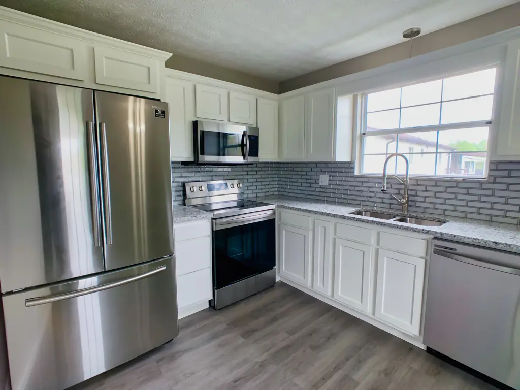 Finished kitchen at the Foxboro Drive project, with white cabinets, gray tile backsplash and stainless appliances
