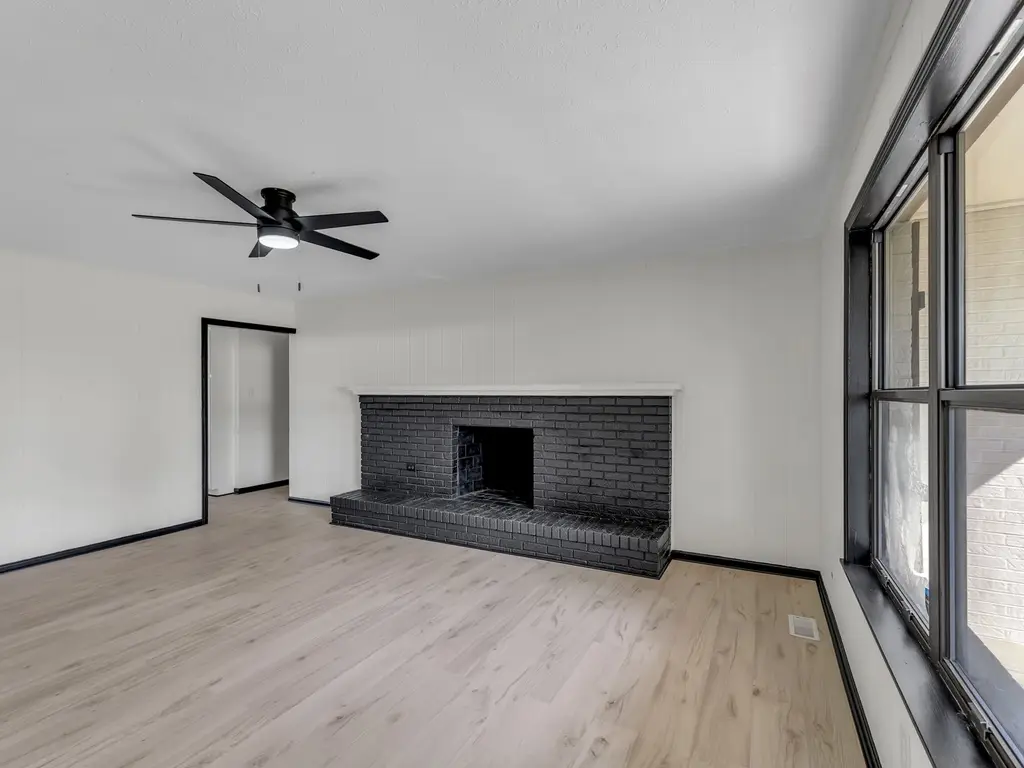 The same Millstone Drive living room after renovation, with white walls, light flooring and a black brick fireplace