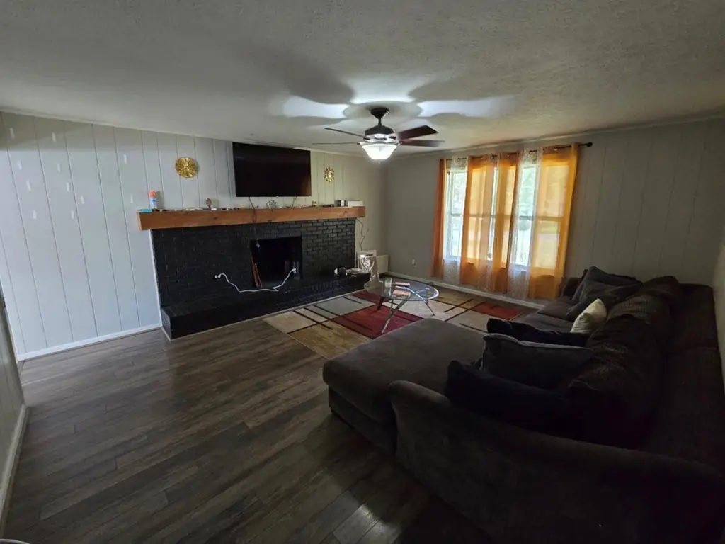 Millstone Drive living room before renovation, with gray paneling, a black brick fireplace, dark flooring and furnishings
