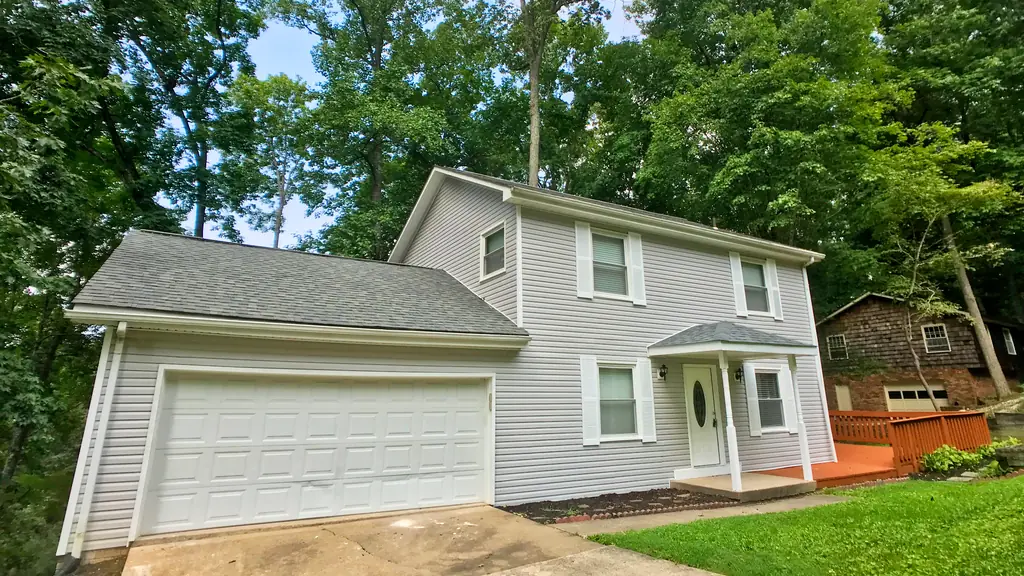 The same Seneca Hills house after renovation, with light siding, covered entry and wood deck