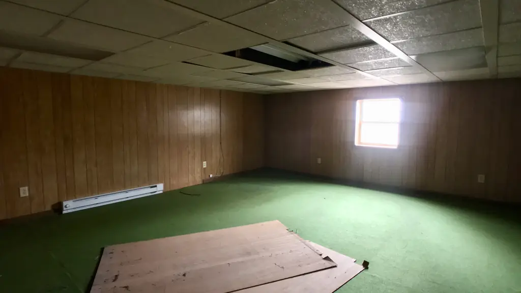 Interior at the Seneca Hills house before work, showing wood paneling, green flooring and missing ceiling tiles