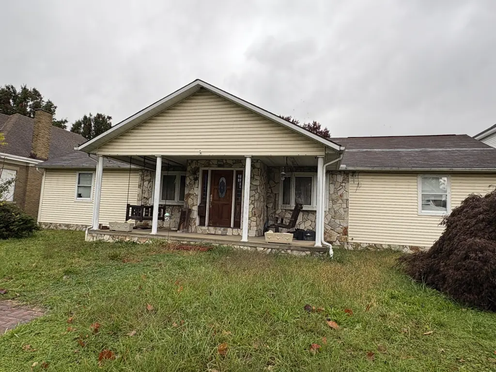 Front of the Collis Avenue house in Huntington before renovation, with stone porch walls, pale siding and an overgrown lawn