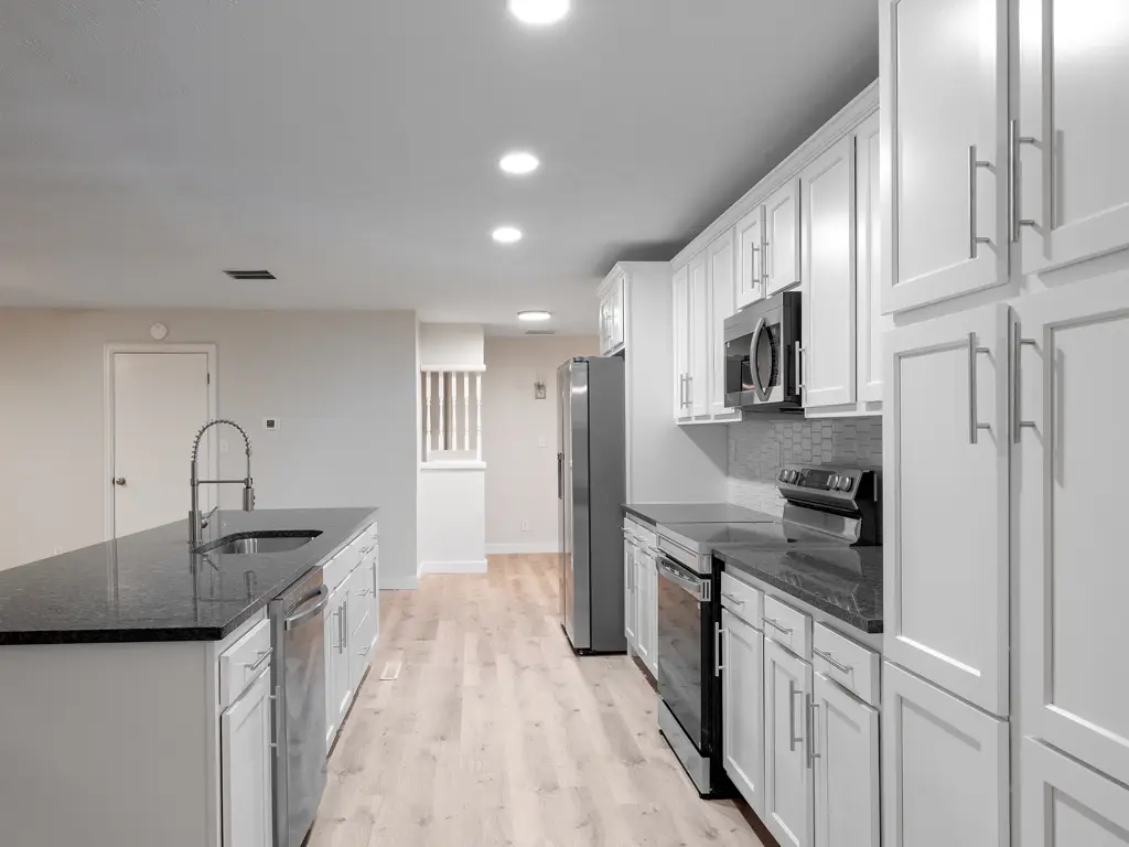 Renovated kitchen at the Collis Avenue property, with white cabinets, a dark island countertop and stainless appliances