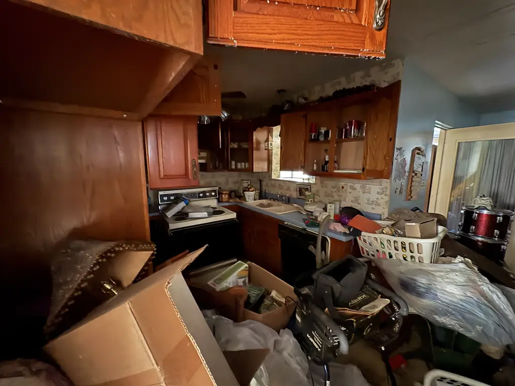 Collis Avenue kitchen before renovation, with wood cabinets, a black range and stored belongings