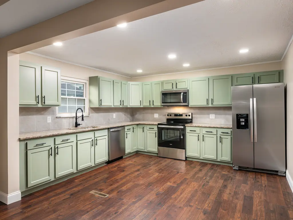 Renovated kitchen at the same Dudding property, with green cabinets, stainless appliances and wood-look flooring