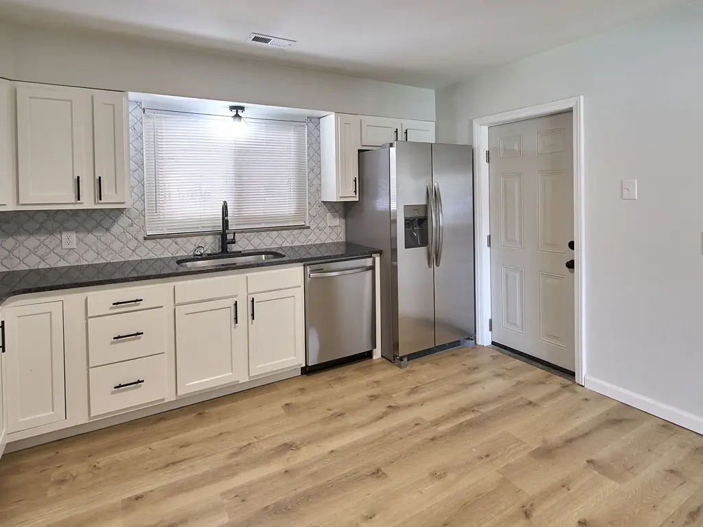 Renovated kitchen at the same Hallison Circle property, with white cabinets, dark counters and stainless appliances