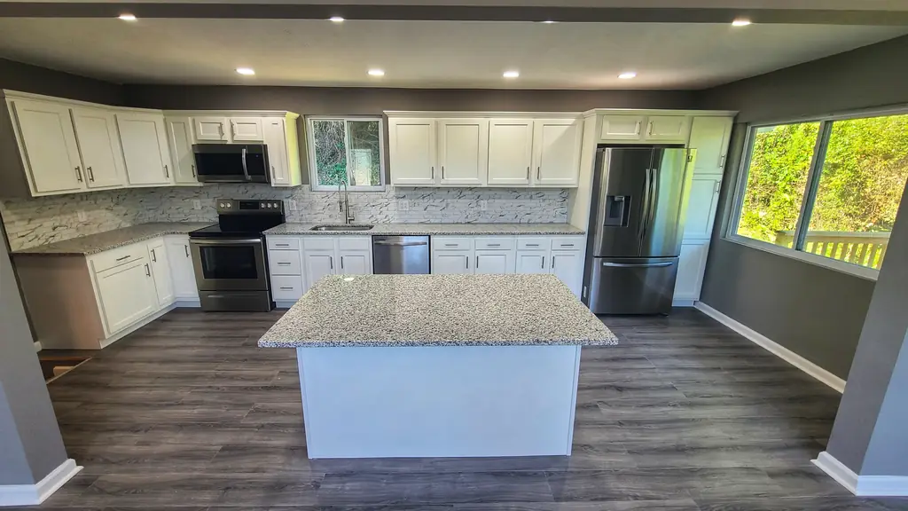 Renovated kitchen at the same Pawnee Drive house, with white cabinets, island, stainless appliances and finished flooring