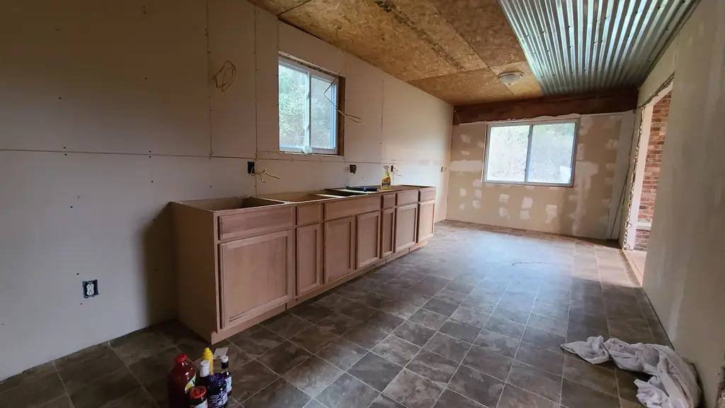 Unfinished kitchen at the Pawnee Drive house before renovation, with bare cabinets, unfinished drywall and exposed ceiling finishes