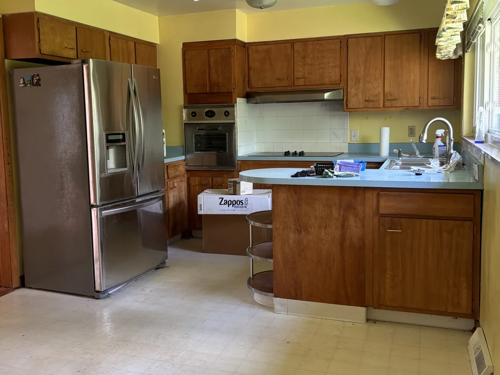 Kitchen at 1212 Crown Drive in South Charleston, WV, before renovation, with wood cabinets, light counters and dated flooring