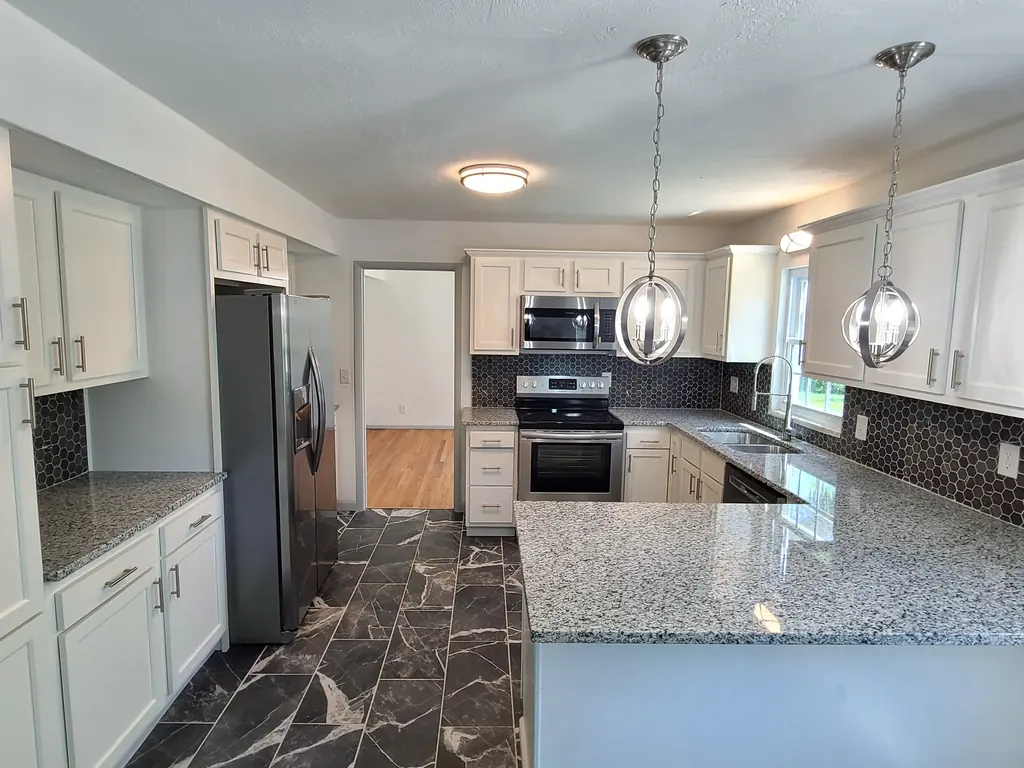The same Lee Street kitchen after renovation, with white cabinets, stone counters, dark backsplash and stainless appliances