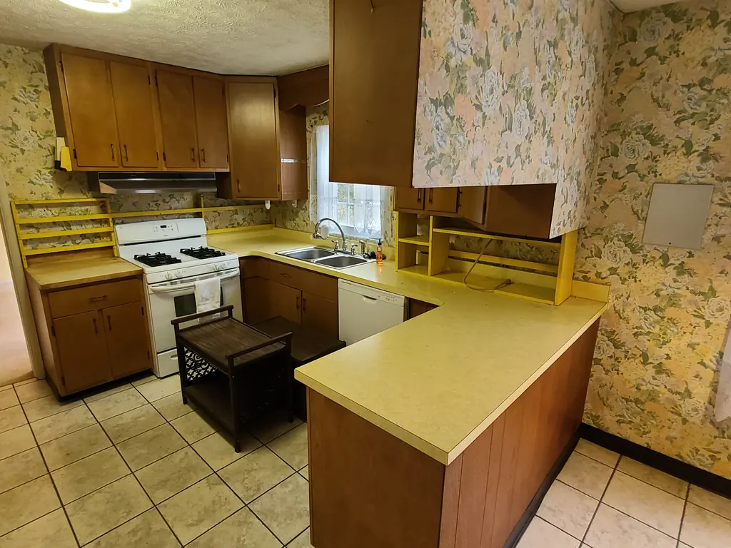 Kitchen at 60 Lee Street in St. Albans before renovation, with wood cabinets, floral wallpaper and yellow counters