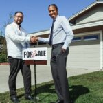 Two people shaking hands in front of a house, next to a sign showing the house has been sold