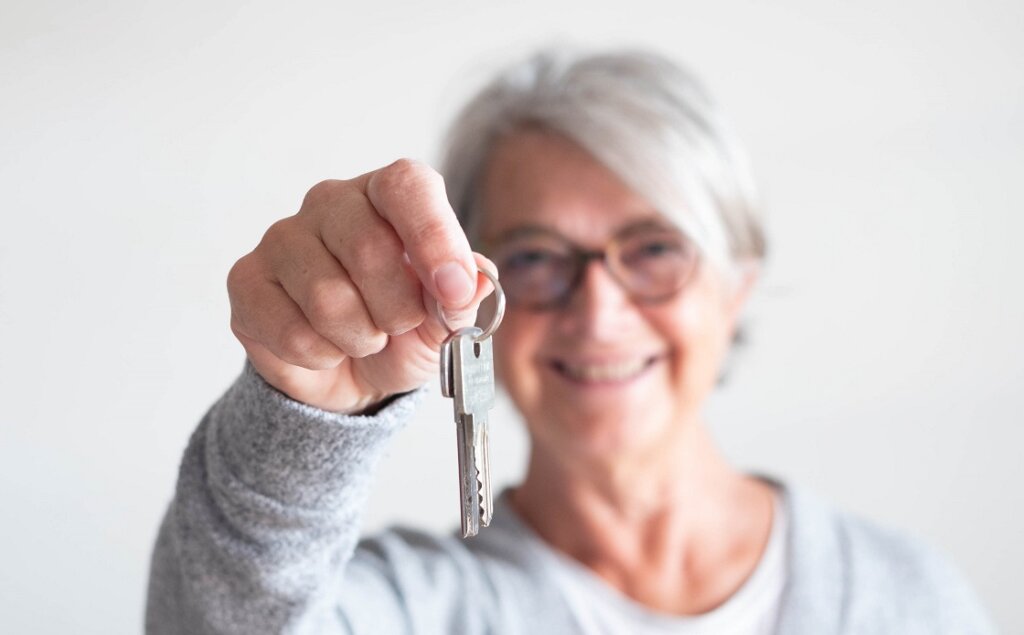 close up of mature woman holding a couple of keys of her new house or home or some property - indipendent senior
