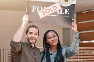 Happy couple holding a "Sold" sign in front of their home