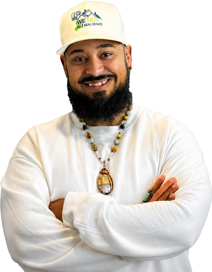 Close-up portrait of Samuel Colon smiling with folded arms, wearing a white sweatshirt and a "We Buy NJ Real Estate" baseball cap.