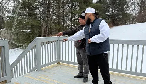 Real estate investors evaluating an exterior wooden deck and railing during a house walkthrough.