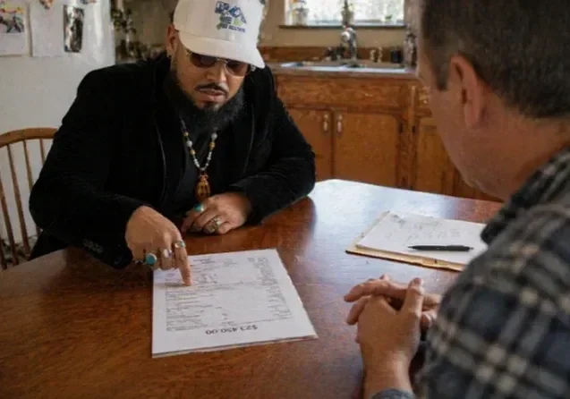 Licensed New Jersey Real Estate Sales Agent Samuel Colon sitting at a wooden table and pointing directly at contract terms while explaining ethical selling options to a client.