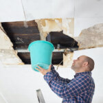 Man Collecting Water In Bucket From a water damaged Ceiling