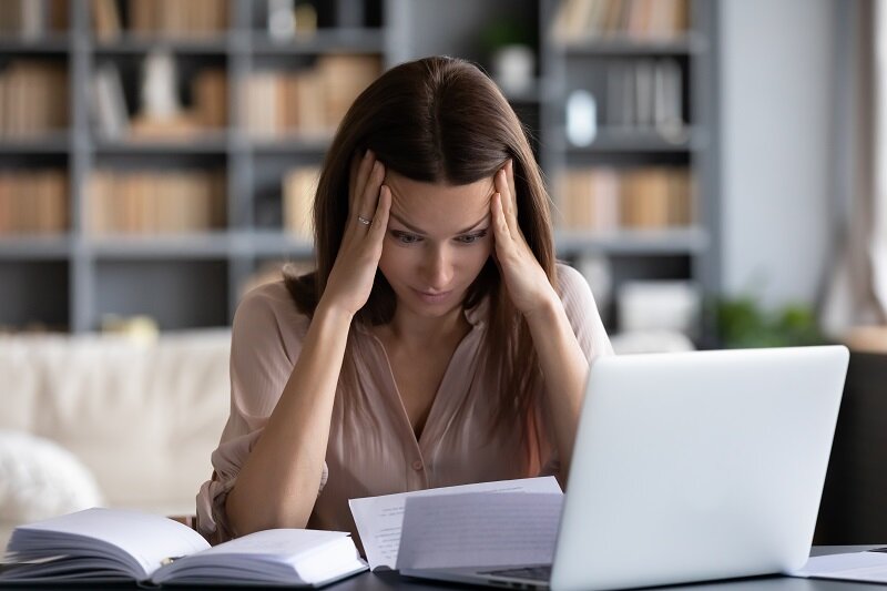 A young homeowner presses her temple while researching how to stop a foreclsoure auction immediately