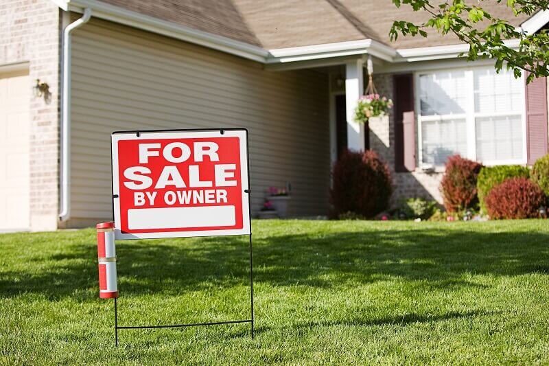 A house with a white and red 'For sale by owner' sign