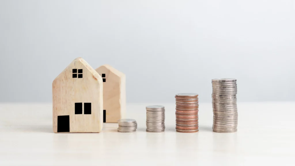 Two small wooden house models sit beside four ascending stacks of coins, symbolizing increasing savings or investment—just like when you sell with We Buy Houses Fort Worth – Sell Without the Stress. All set against a plain white background.