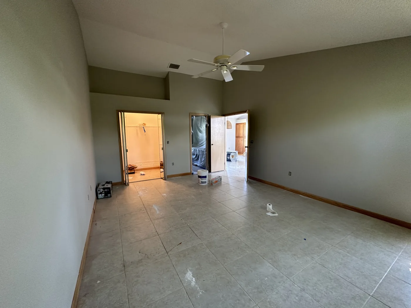 Mostly empty tiled living room with a ceiling fan and a few belongings
