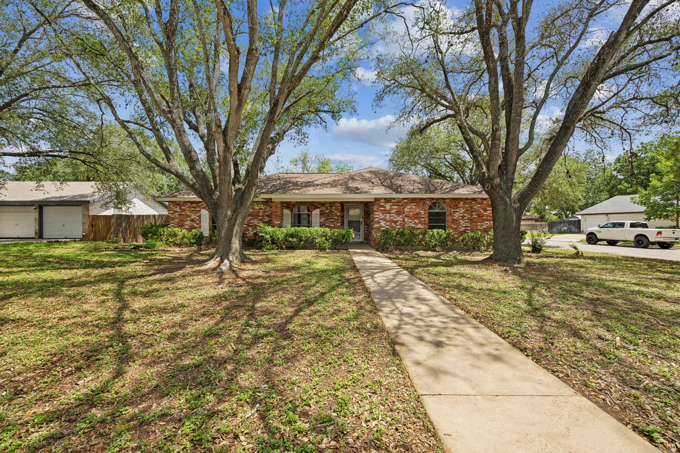Brick home behind mature trees and a front walkway