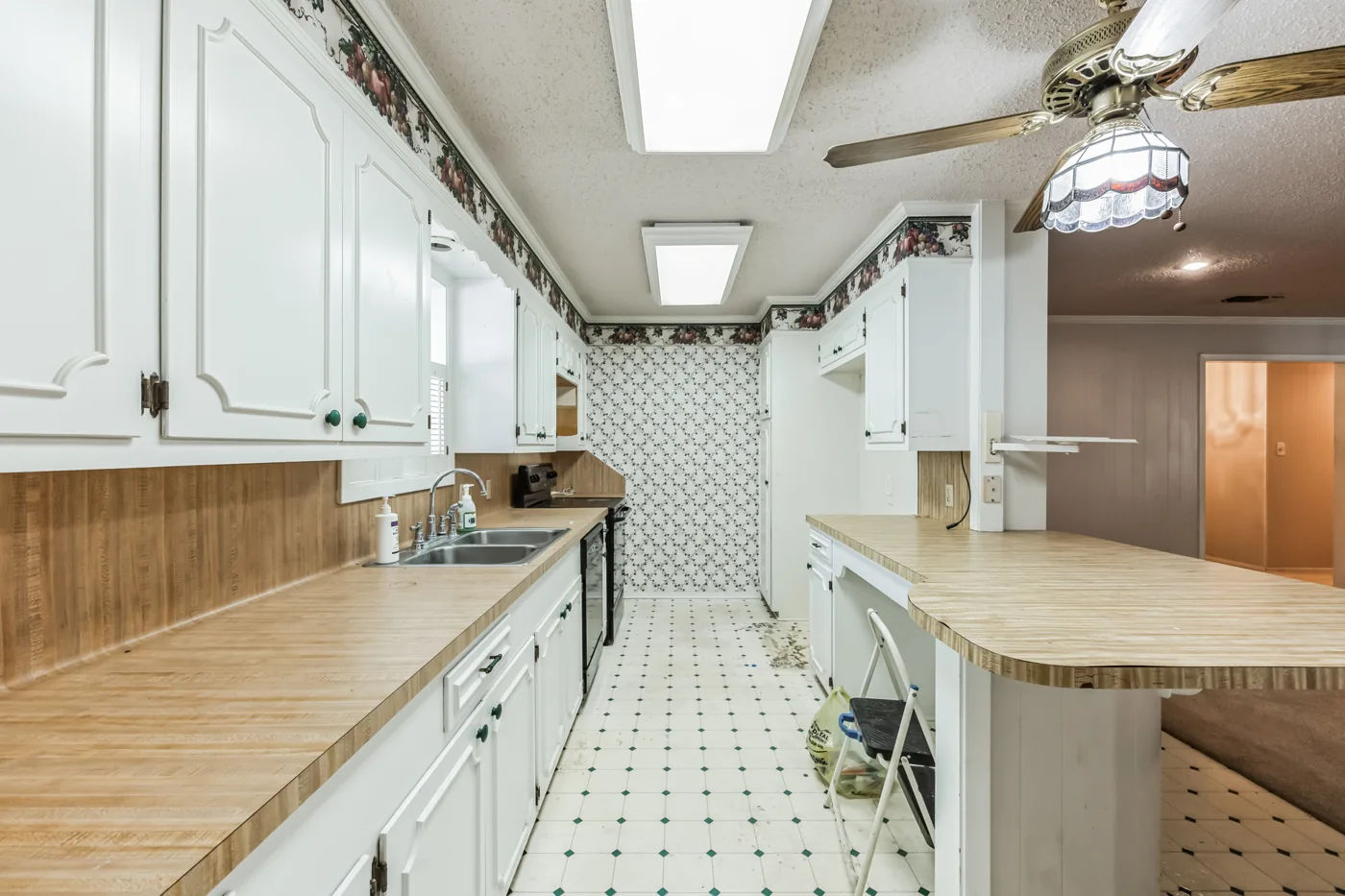 Kitchen with white cabinets, counters and patterned wallpaper
