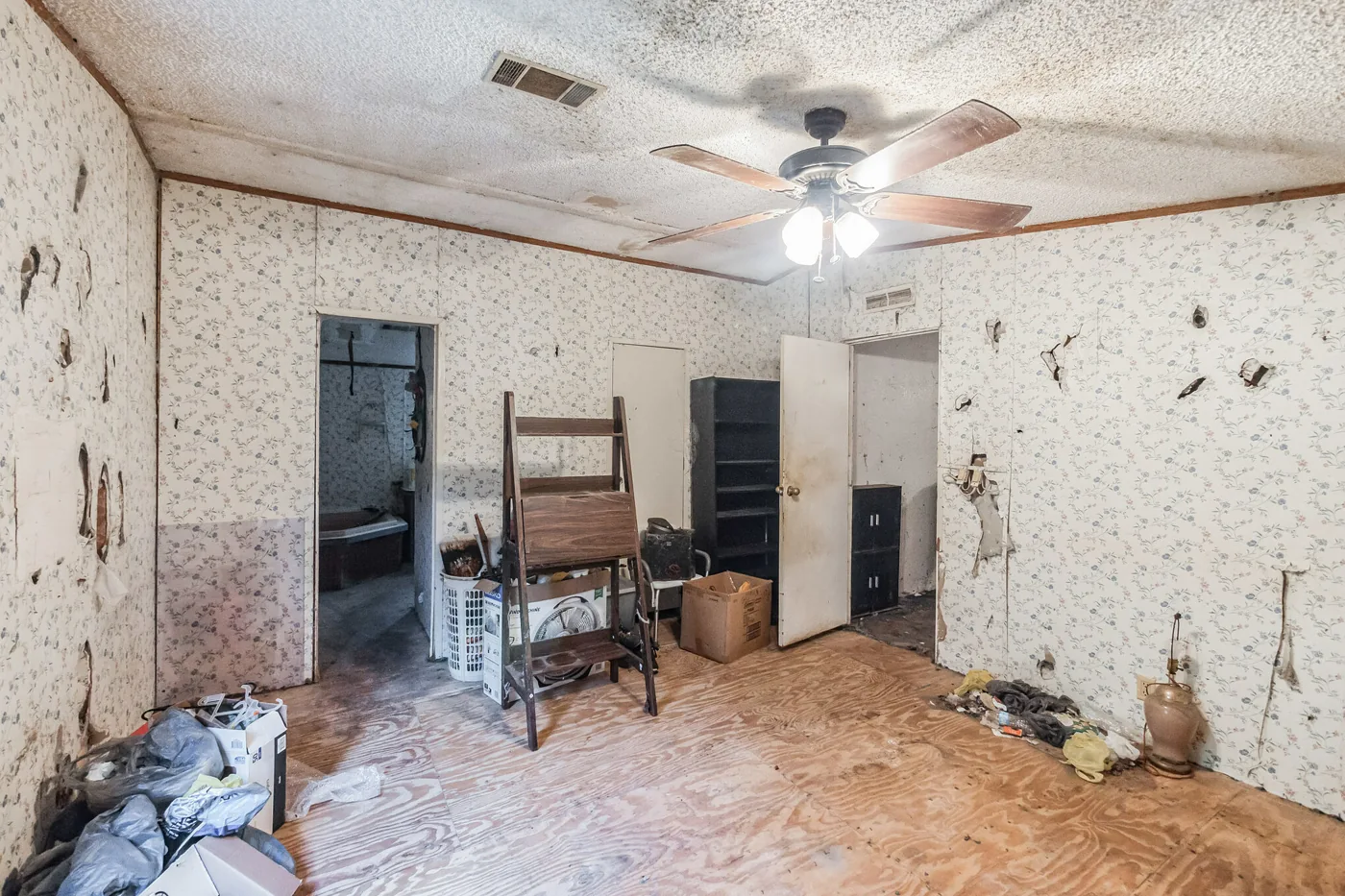 Interior room with wall damage, bare flooring and belongings