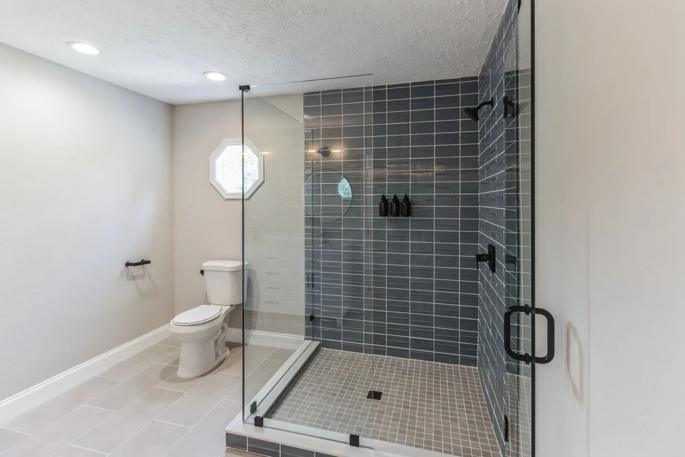 Renovated bathroom with a glass shower enclosure and dark wall tile