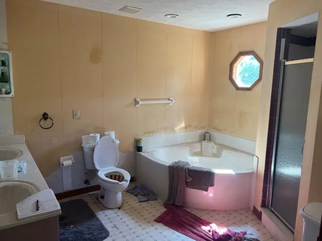 Bathroom before renovation with a corner tub, toilet and unfinished wall areas