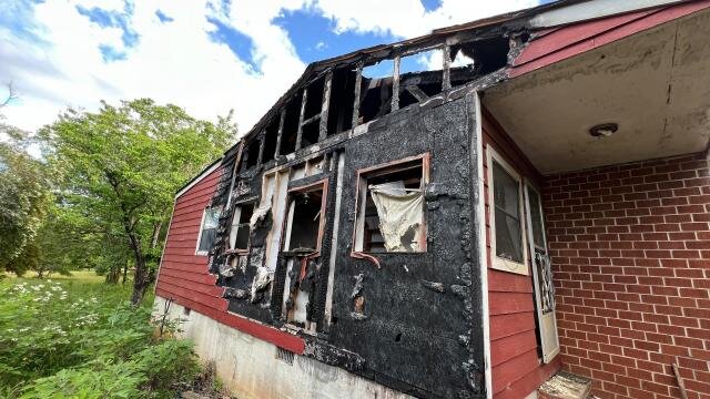 Fire-damaged side wall at 517 Denton St, with charred framing and damaged windows