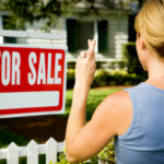 woman and for sale sign with house as background