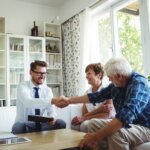A young home investor shakes hands with a couple of senior homeowners