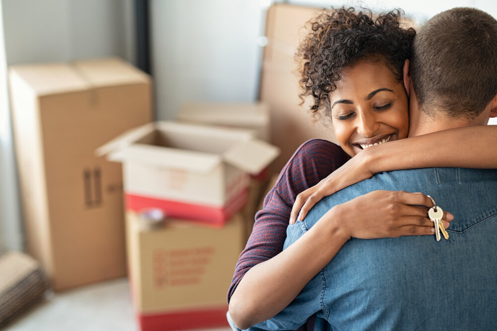 Young african woman holding home keys while hugging boyfriend in their new apartment after buying real estate.