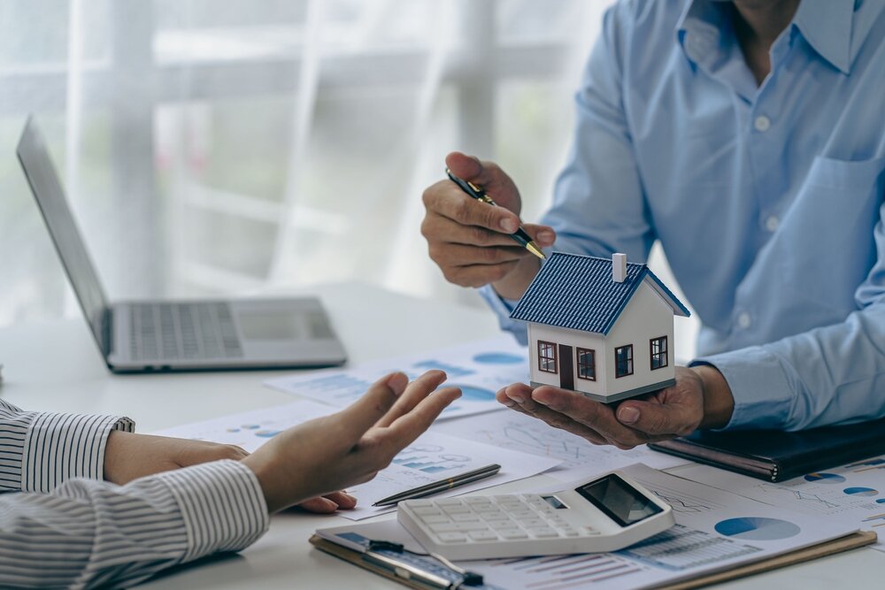 eal estate agent with house model talking to client about buying home insurance and client signing contract under formal contract agreement with real estate law