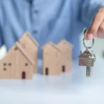 Hand working at home with Buy or Rent, copy space. Real estate investment and home mortgage financial concept, Hand putting gold coin stacked with wooden house.