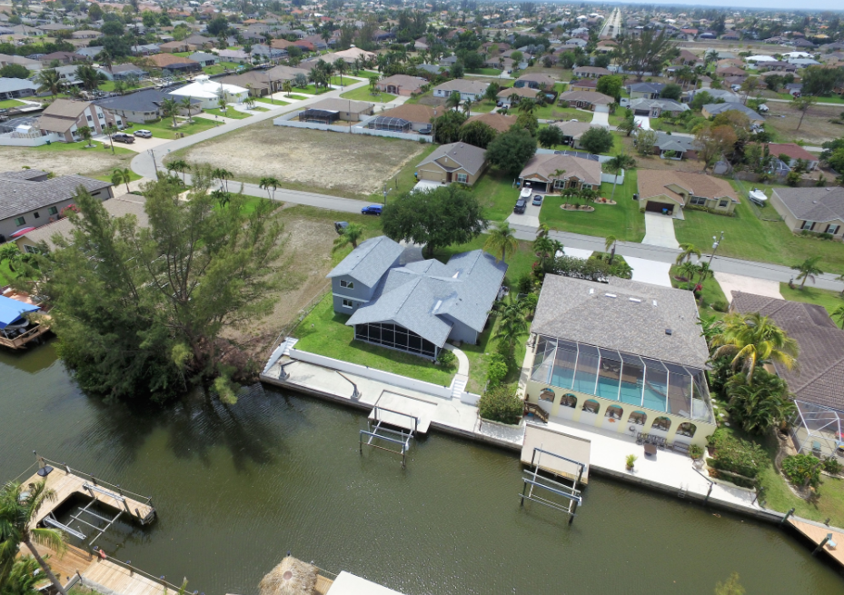 Drone image of fort myers foreclosure sale above the house and showing a canal and some trees and the horizon and showing local amenities and schools and the street and things that are important to a real estate foreclosure sale buyer that is looking for real estate deals and to sign up for real estate deal information