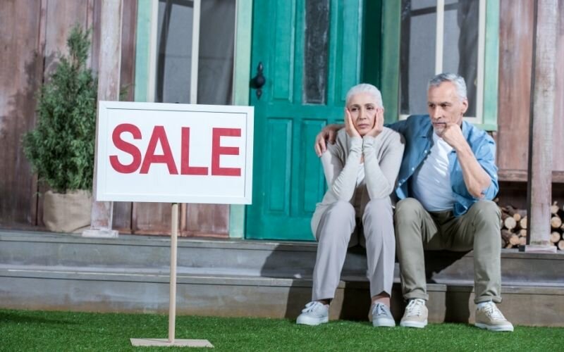upset senior couple sitting on porch and selling their house