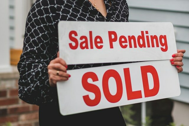 A woman in a black shirt replacing a white and red sale pending sign with a white and red sold sign in front of a South Carolina house