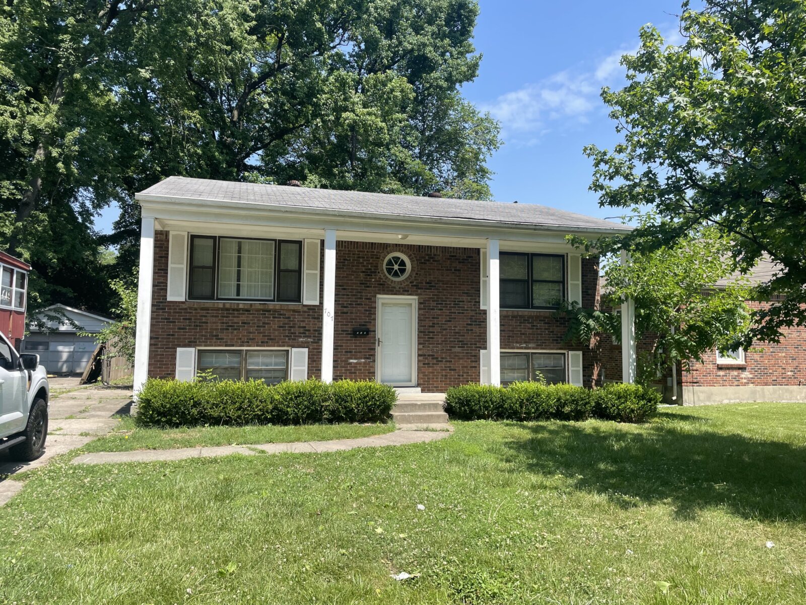 Brick home with white columns, a green front lawn and leafy trees under a blue sky