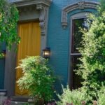 Typical Victorian Home in Old Louisville with lush landscape with Yellow front door and blue green paint over brick accented with Grey trim.