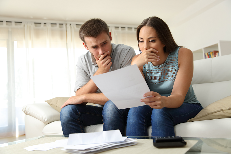 A worried couple sitting on a couch and reading the costs of selling their home