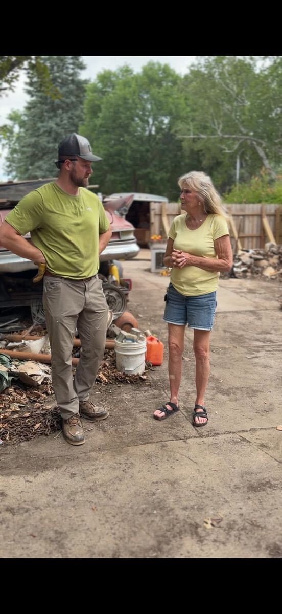 Two people talking outdoors beside a driveway.