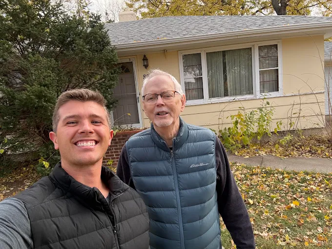 Two adults outside a yellow house, from Dakota Home Buyers’ Google business profile