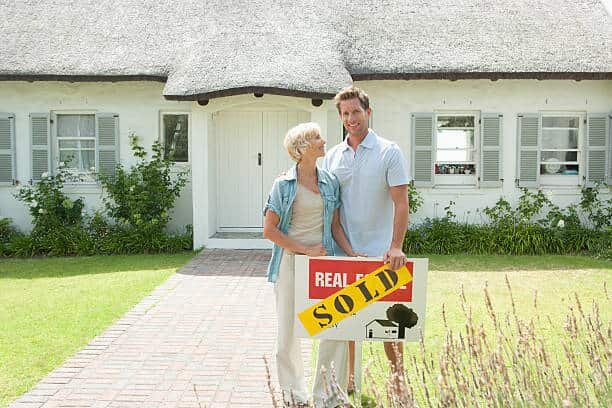 Happy couple holding a “Sold” sign in front of their fixer-upper house in Fresno, CA – Cash home buyers, sell my house fast Fresno, we buy houses as-is