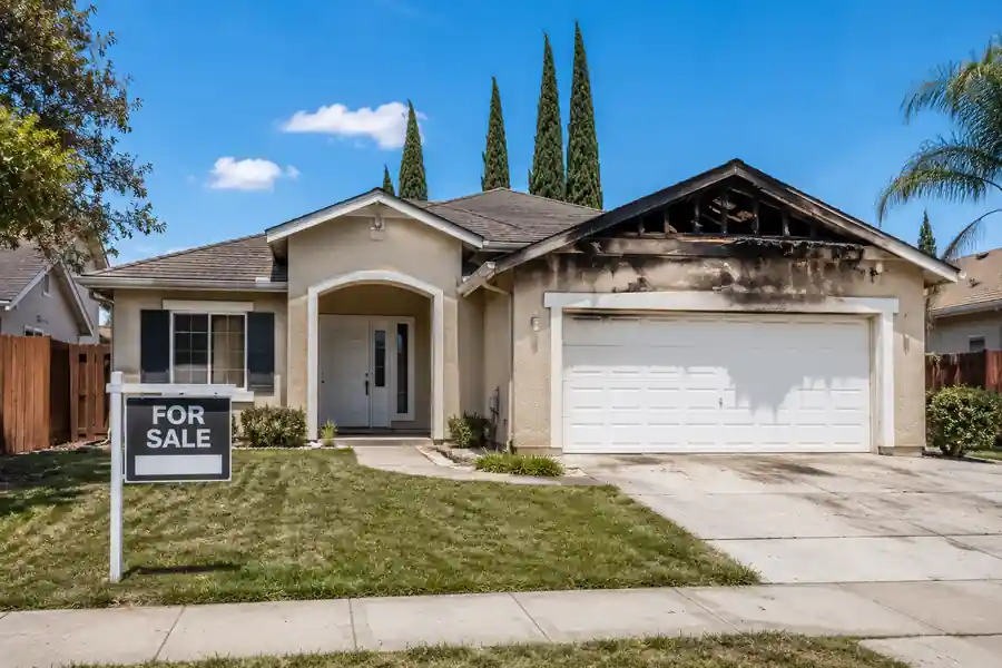 Exterior of a fire-damaged house in California with visible smoke damage near the roofline, representing a property being prepared for an as-is cash sale.