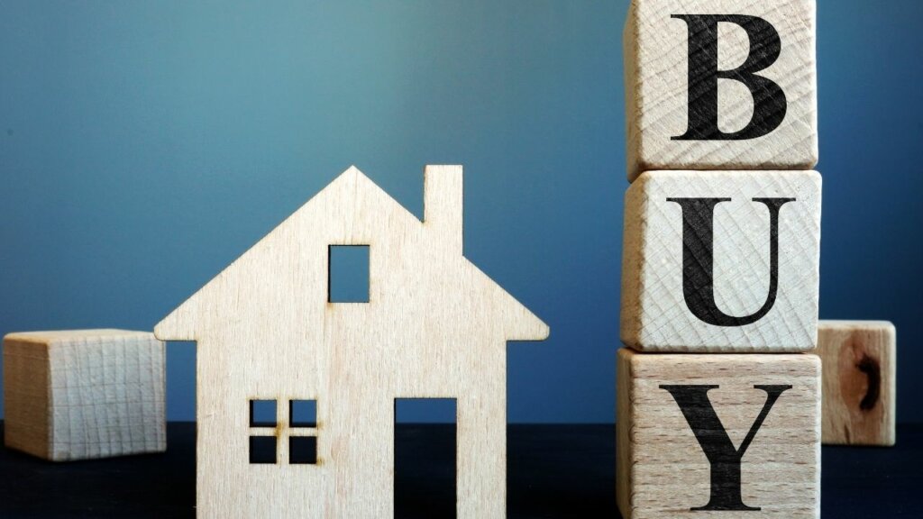 wooden blocks, one is shaped as a house, three square blocks are stacked on top of each other and spell BUY